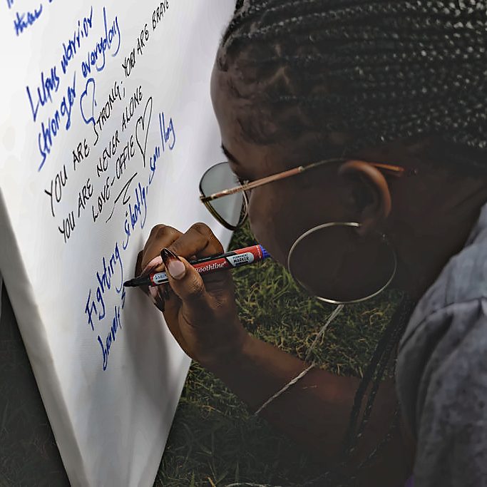 A community member writing a message of hope on the World Lupus Day pledge wall